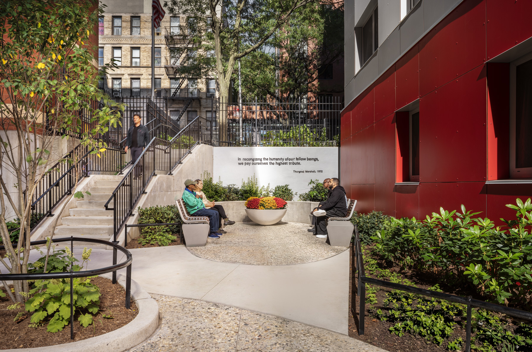 NYCHA PACT Marshall Plaza Courtyard Gathering Space with Thurgood Marshall Quote Residents gathered in courtyard seating area at NYCHA PACT Marshall Plaza featuring Thurgood Marshall quote wall and landscape design in Washington Heights, Manhattan.