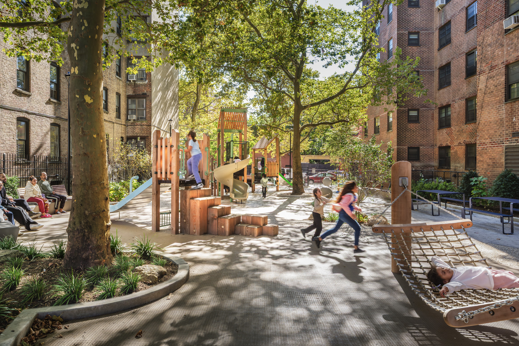 Children playing in inclusive playground at NYCHA PACT Audubon Houses with natural play elements and shaded landscape design in Washington Heights Manhattan